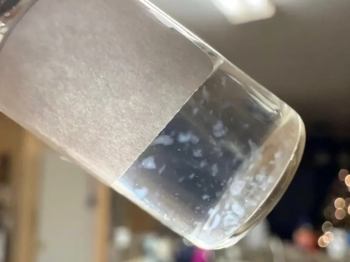 A vial held up to the light, its liquid clouded with floating particles
